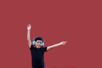 9 year old Latino dark-skinned boy listens to music on his headphones and dances excitedly pointing...