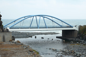 Pedestrian arch bridge at the confluence of a narrow rocky river into the ocean. Madeira Island.