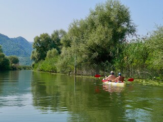 Fototapeta na wymiar Kayaking on beautiful Skadar lake surrounded by green mountain peaks. Skadar Lake National Park, Montenegro.