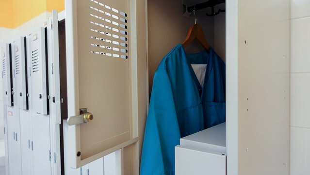 Open metal lockers in the locker room. A nurse's clothes, turquoise smocks and trousers, are hanging on a hanger. Concept of acute shortage of care staff and doctors in hospitals and nursing homes.