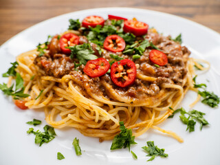 Spaghetti Bolognese dish with pasta, red sauce, minced beef, red peppers and green fresh herbs on white plate and light color table cloth. High quality products in a tasty Italian style dish.