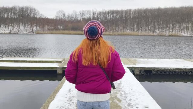 Leisure walk near lake on cold winter day. Woman wearing colorful knit hat is relaxing near lake on cold winter day
