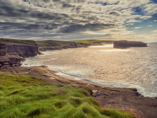 Stunning Irish scenery landscape with ocean, rough stone coast, cliff and small island. Low cloudy sky. Kilkee area, Ireland. Travel and sightseeing concept.