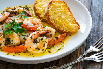 Fried shrimps with garlic and parsley in olive oil and toasted bread with parmesan cheese on wooden table