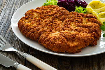 Crispy breaded fried pork chop with potato puree and cooked red cabbage on wooden table