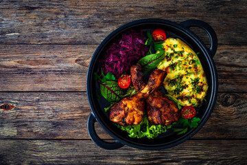 Baked chicken drumsticks with red cabbage and potato puree on wooden table
