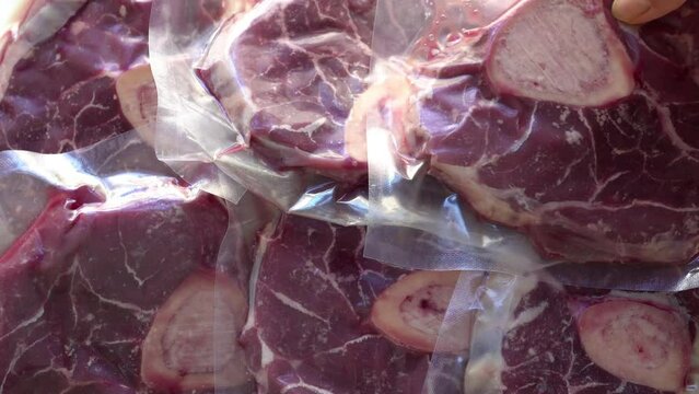 たくさんの骨付き牛肉の真空パックを並べる女性の手のクローズアップ　俯瞰撮影