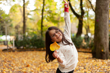 Little girl in the autumn park with a yellow leaf in her hand