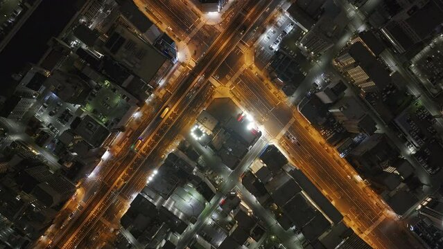Top down footage of vehicles driving on thoroughfare in night city. Orange color streetlights along road and intersection. Osaka, Japan