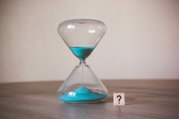 hourglass with a question mark written on a wooden cube. Time management concept. Word "?" next to an hourglass. the concept of interrogation. concept of an enigma