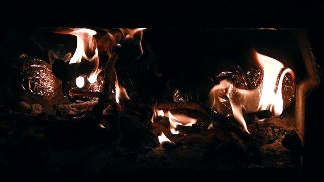 Bright orange flames flickering inside a dark fireplace during a cold winter evening at home. Close up view of burning wood logs glowing and dancing fire light i creating a cozy atmosphere