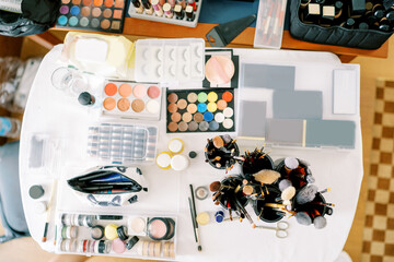 Large table with sets of cosmetics and makeup brushes. Top view