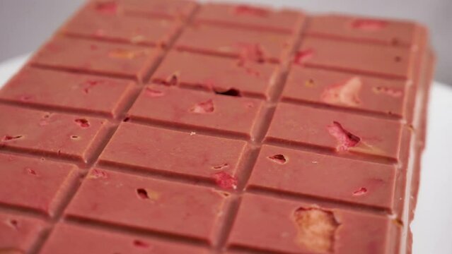 A bar of pink ruby chocolate with freeze-dried strawberries and almonds close-up. A healthy dessert based on berries and nuts