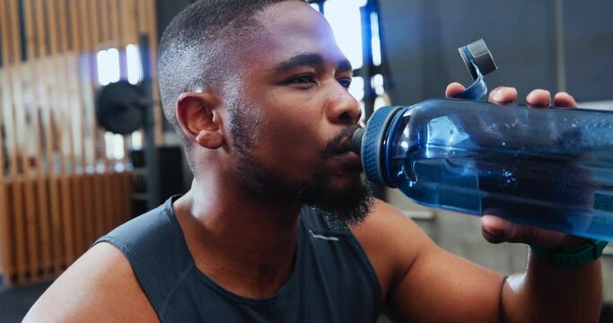 Black man, drinking water and bottle in gym for fitness, health and hydration with lens flare and wellness. Thirsty after workout, exercise and h2o liquid, training or sports with athlete at club