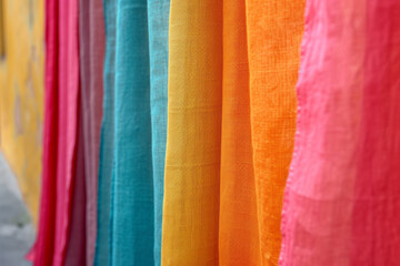 Row of colorful luxurious textiles hanging on the rack. Natural fabrics of different vibrant colors. Creative background. Close-up.