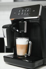 Modern coffee machine with glass cup of latte on white marble countertop in kitchen