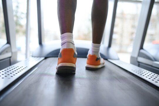 Back view of unrecognizable male legs running on treadmill in gym.