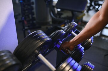 Close-up man grabs a heavy dumbbell in gym with his hand. Concept lifting, fitness