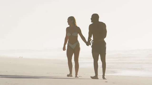 Full length shot of loving young couple wearing swimwear holding hands and walking along beach in South Africa - shot in slow motion