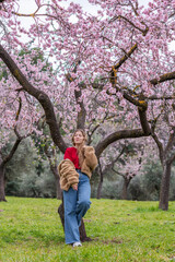 25 year old Caucasian girl with curly blonde hair posing next to blooming almond trees.