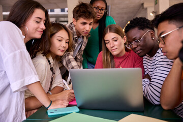 Group of young classmates studying together using laptop in the classroom at university campus. Academic multiracial people working in a project with serious face on the faculty. Education online