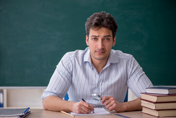Young male teacher in front of green board
