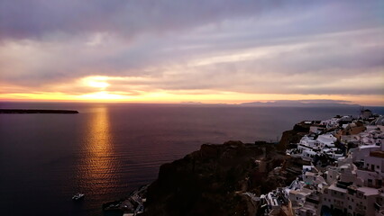 Fototapeta premium Santorini, Greece - 03.31.2018: Sunset in Oia with traditional houses on the cliff towards Aegean Sea