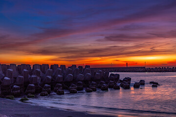 Stunning sunset blues hour view. Magnificent, beautiful breakwater, red cloudy sky form a scenic...
