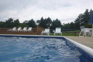 pool deck area with pool view, lounge chairs, and trees in the background  