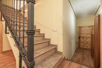 Interior staircase of a duplex residential house with gray tile steps, metal railing and Castilian-style paneled wooden access door