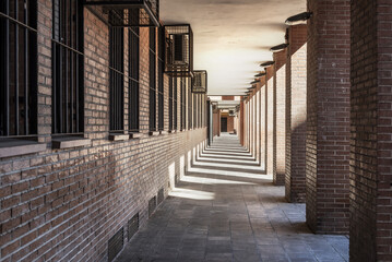 Passage on the ground floor of a brown brick building with shadows of the pillars, vanishing point...