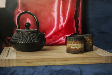 An Asian style black wrought iron jug with some tea glasses next to it on a bamboo board with a red...