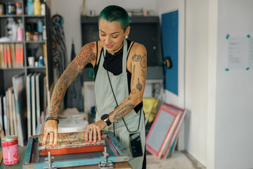 Female worker with squeegee is printing images on textile by silkscreen method in a design studio