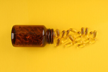 Glass medical bottle and vitamin capsules on yellow background, top view