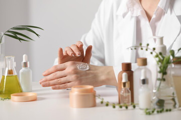 Dermatologist applying cream onto hand at white table indoors, closeup. Testing cosmetic product