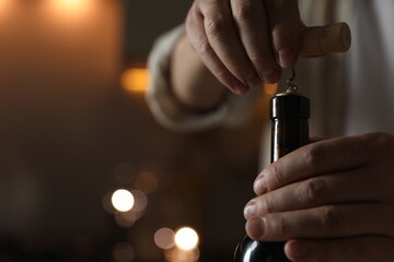 Man opening wine bottle with corkscrew on blurred background, closeup. Space for text