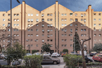 Peculiar facade of urban residential buildings on a street with trees and hedges between cars