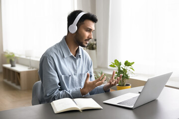 Serious Indian man in headphones lead on-line communication using laptop and video call...