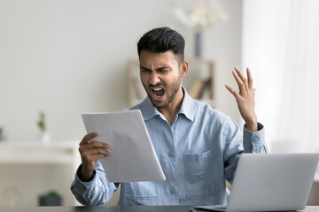 Angry Indian man holding documents, read awful news, get bank debt notice, distressed by negative...