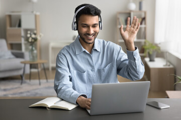 Young Indian man sit at desk wear wireless headphones greets teacher start video call lesson to gain new knowledge, learn language, studying online, using laptop and modern videoconference application - obrazy, fototapety, plakaty