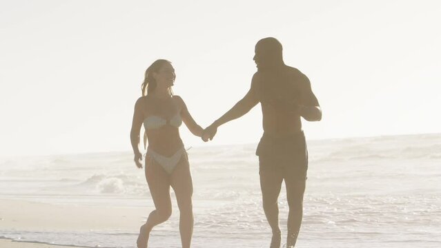 Three quarter length shot of loving young couple in swimwear holding hands and running along beach in South Africa - shot in slow motion