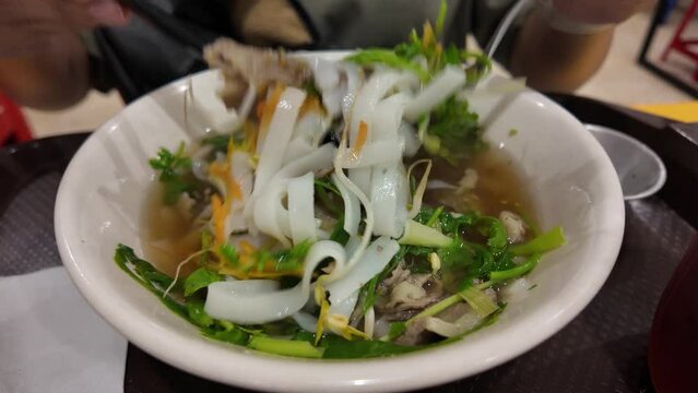 Asian woman eating Vietnamese soup dish Pho that consisting of broth, rice noodles, herbs, and beef pork chicken meat with scallion, onion, cilantro (coriander leaves), bean sprouts, lime, chili oil.