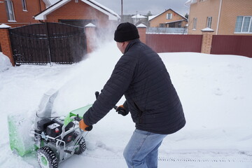 A man cleans snow in the winter in the courtyard of the house,  man cleaning snow with a snow blower