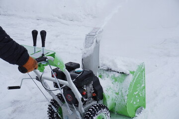A man cleans snow in the winter in the courtyard of the house,  man cleaning snow with a snow blower