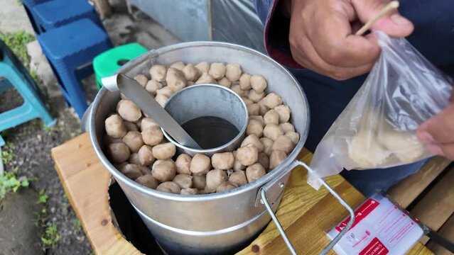 Indonesian street food pentol seller is serving customers that order take away food.