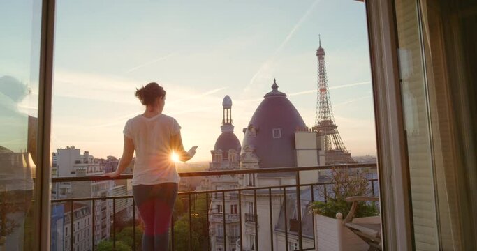 Woman, sunrise and smartphone on balcony in hotel for checking weather, daily news or social media in Paris. Back view, morning and female person outdoors for travel, holiday and accommodation