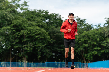 Attractive Young indian man wearing sportswear running on track at sport stadium. Asian Fit man jogging outdoor cross the finish line. Exercise in the morning. Healthy and active lifestyle concept.