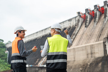Confident asian two maintenance engineers man inspection discussstion with tablet at construction site dam with hydroelectric power plant and irrigation. Team engineer man working at project - obrazy, fototapety, plakaty