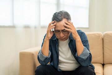 Asian mature old man sitting headache tired on sofa at home. Portrait of serious depression sadness...