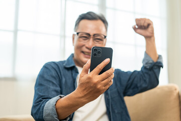 Handsome asian mature old man using smartphone on sofa in living room at home. Happy Portrait of cheerful smiling senior asian man holding cell phone. Mature People and lifestyle